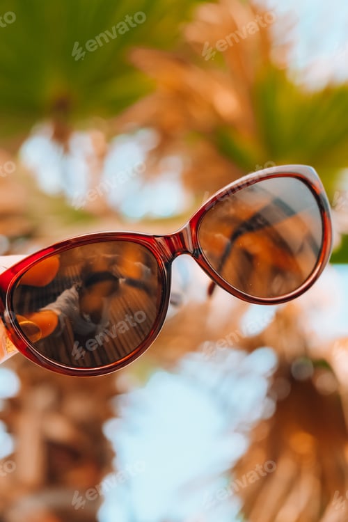 Preview: Woman holding Sunglasses on tropical palm leaves background. Summer concept. paradise beach vacation
