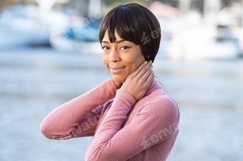 Preview: Beautiful African American with black hair bangs outside near lake wearing pretty pink sweater