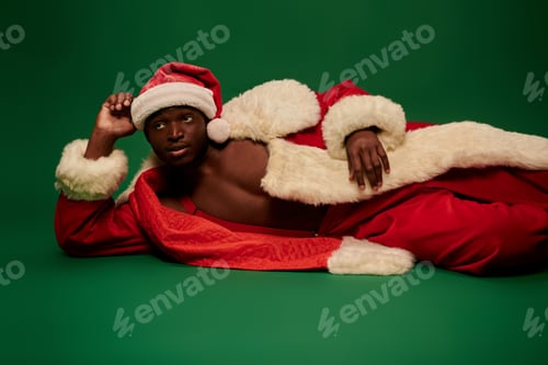 Preview: sexy african american man in santa costume on shirtless body laying down and looking away on green