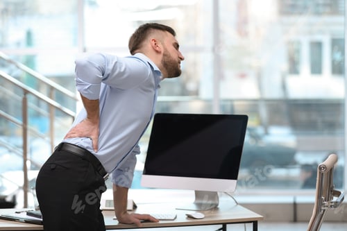 Preview: Businessman suffering from back pain at workplace