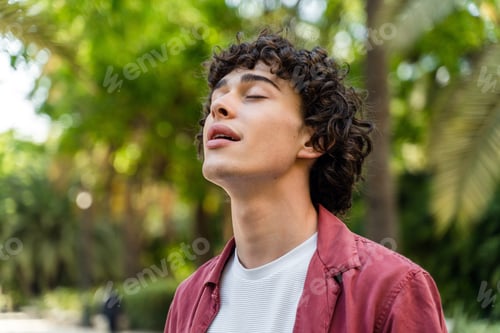 Preview: Young man standing with closed eyes and pleasure smile while walking outdoors