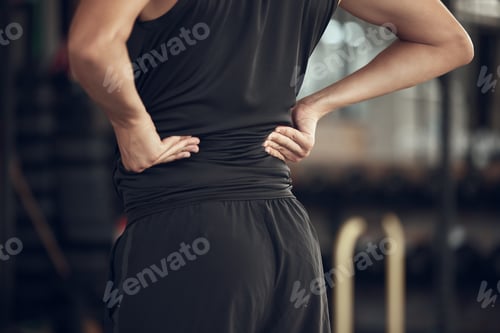 Preview: Fit man experiencing back pain in the gym. Athlete with a sore back in the gym. Bodybuilder with ba