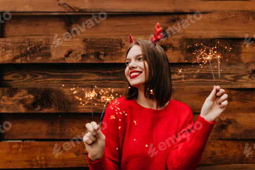Preview: Pleasant girl in winter red sweater holding bengal light. Outdoor shot of happy european lady with