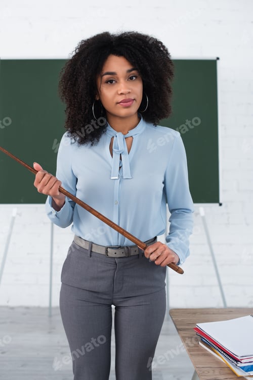 Preview: African american teacher holding pointer near notebooks in classroom