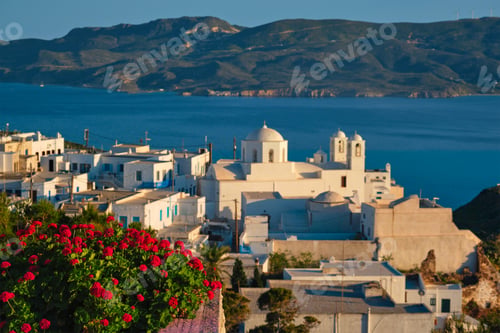 Preview: View of Plaka village on Milos island over red geranium flowers on sunset in Greece