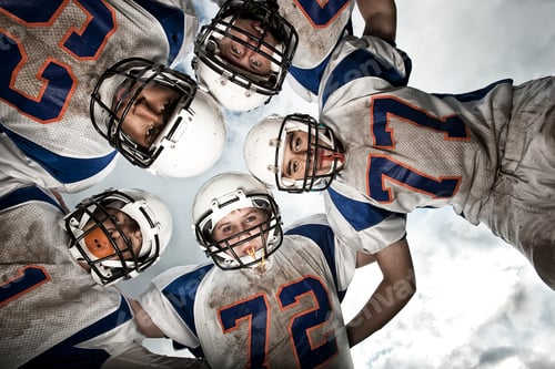 Preview: A group of football players in a team huddle viewed from below.