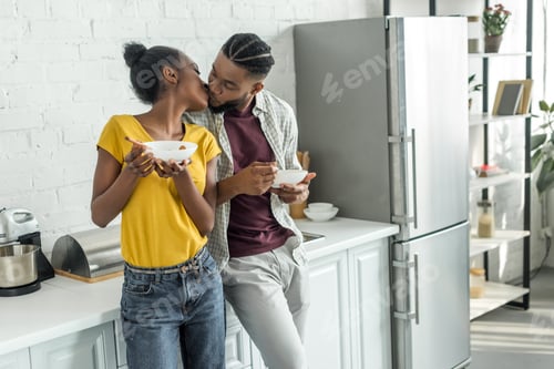 Preview: african american couple kissing while having breakfast at kitchen
