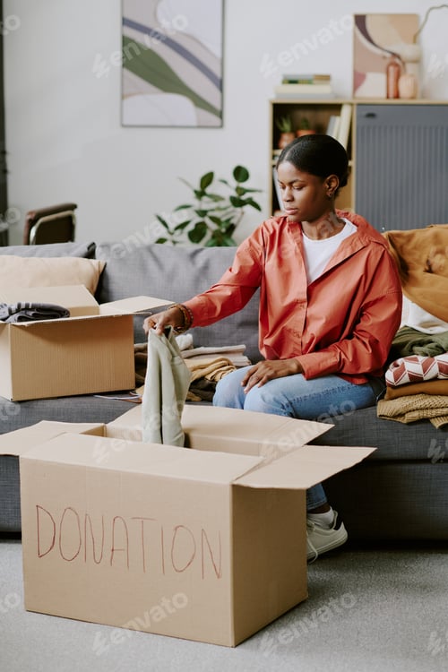 Preview: Black Woman Sorting Clothing Donations for Charity Drive at Home