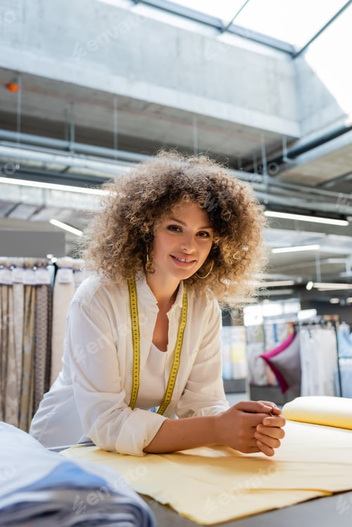 Preview: joyful saleswoman with measuring tape smiling near fabric rolls in textile shop