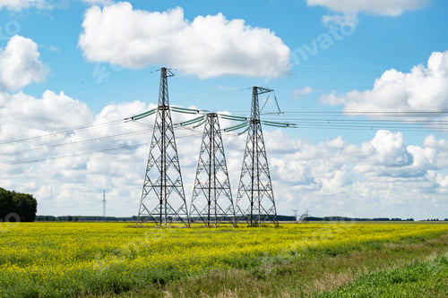 Preview: power line tower against blue sky and clouds over yellow field in summer