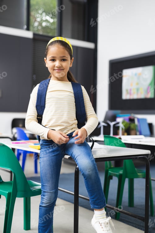 Preview: In school, young biracial girl standing in classroom, wearing a backpack