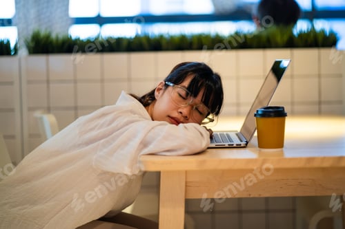 Preview: A woman is sleeping on a table with a laptop and a cup