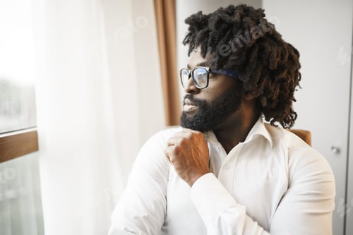 Preview: Black man in formal shirt thoughtfully looking at the window