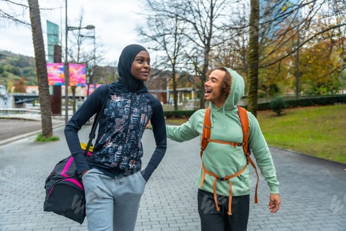 Preview: Diverse young friends walking talking urban park