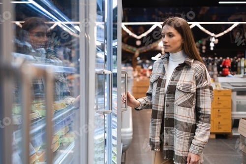 Preview: Woman opens the refrigerator door with a product in a supermarket.