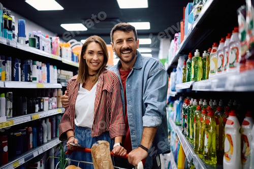 Preview: Happy couple buying in supermarket and looking at camera.