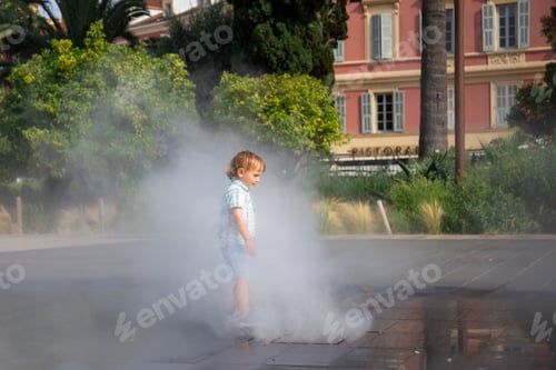 Preview: Toddler boy under spray jets of extensive water mirror fountain in Nice, France.
