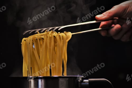 Preview: Closeup of a person holding hot pasta with a spaghetti tong with a dark blurry background