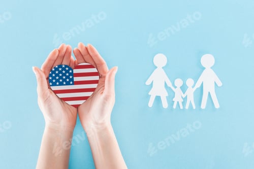 Preview: cropped view of woman holding heart made of national american flag near white paper cut family on