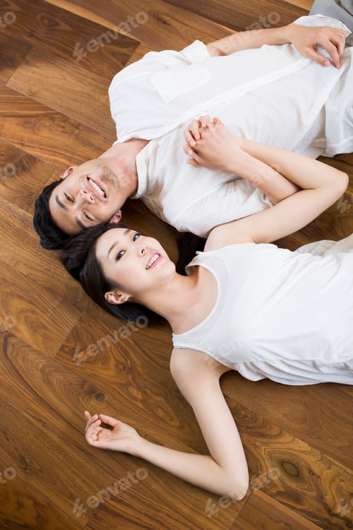 Preview: Young couple holding hands lying on wooden floor