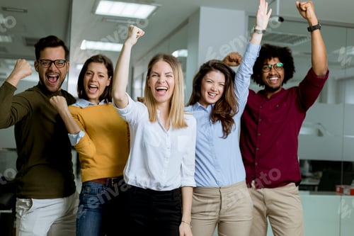 Preview: Group of young excited business people with hands up standing in office