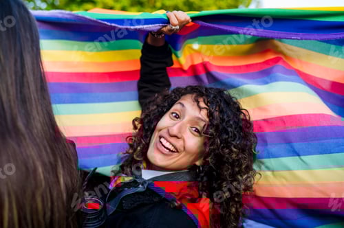 Preview: Woman looking at camera while holding a rainbow flag in an lgbtq pride march.