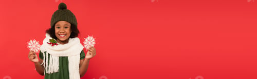 Preview: African american kid with mistletoe on scarf holding decorative snowflakes isolated on red, banner