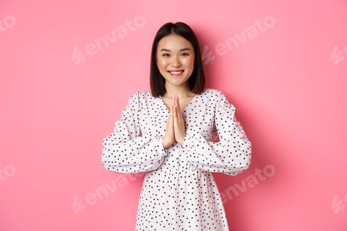 Preview: Beautiful asian woman thanking you, holding hands together in appreciation gesture, smiling happy at