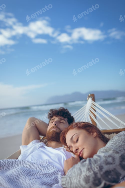 Preview: High angle view of relaxed Caucasian couple sleeping on hammock at beach. Ocean in the background