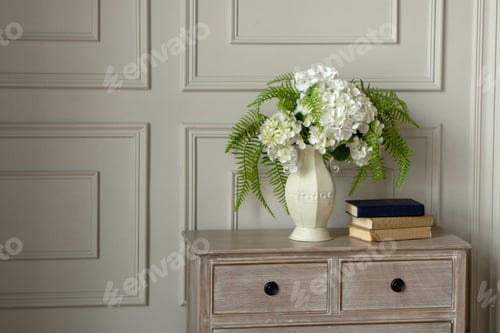 Preview: A white vase with white flowers stands on the dresser against th
