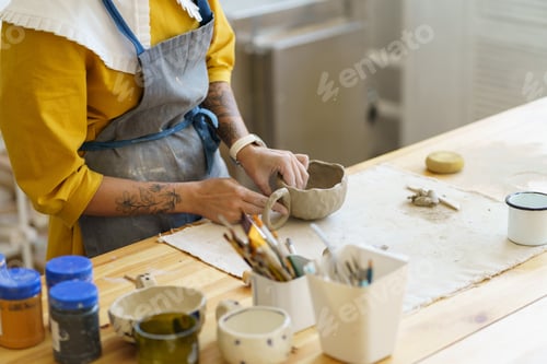 Preview: Woman in apron shaping pottery in art studio, making clay mug during ceramics masterclass