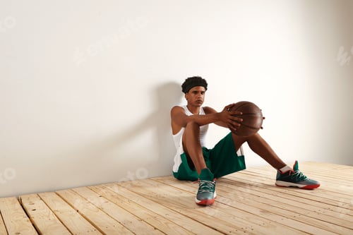 Preview: Tired basketball player sitting on the floor against the wall