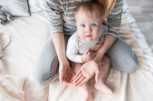 Preview: Top View Of Young Woman With Her Baby Girl Sitting In Bedroom. Little Girl Is Looking At Camera