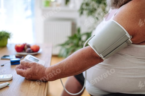 Preview: Overweight man measuring his blood pressure at home.