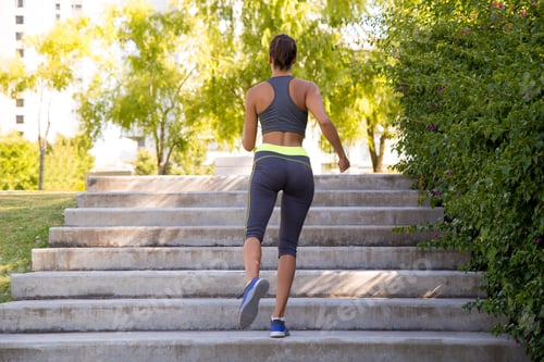 Preview: Hispanic woman in black sportswear working out at a flight of stairs