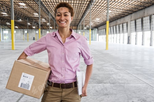 Preview: Black female holding cardboard box and standing in front of loading dock doors in a new empty