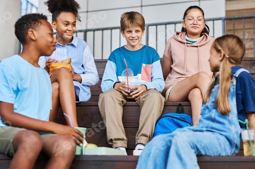 Preview: Group of happy intercultural schoolkids having talk during lunch break