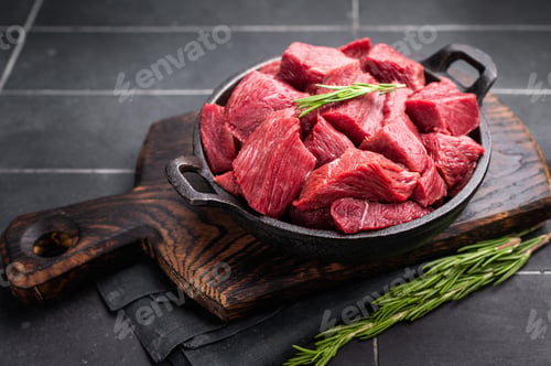 Preview: Diced Raw Ostrich meat, uncooked Game Meat in a skillet. black background. top view