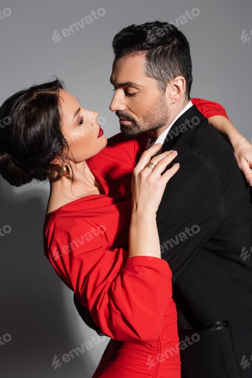 Preview: Sensual brunette woman hugging boyfriend in suit on grey background