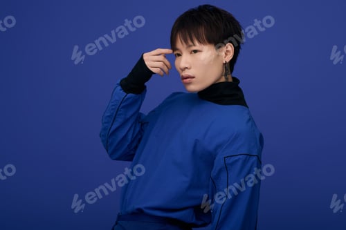 Preview: Striking young asian man poses in bold blue attire against vibrant blue backdrop
