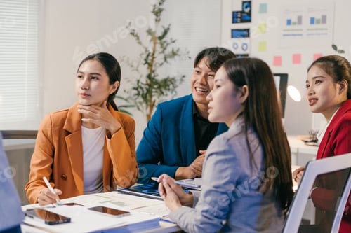 Preview: Four asian businesspeople are sitting around a table in a modern office, listening to a presentation