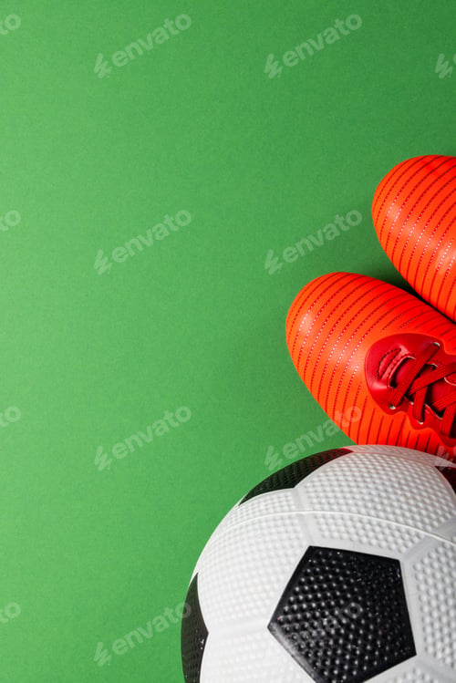Preview: Composition of football and red shoes on green background with copy space