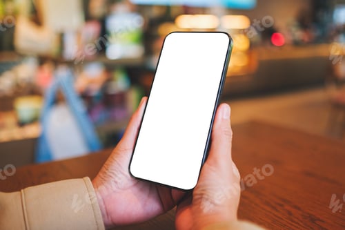 Preview: Mockup image of a woman holding and using mobile phone with blank desktop in cafe