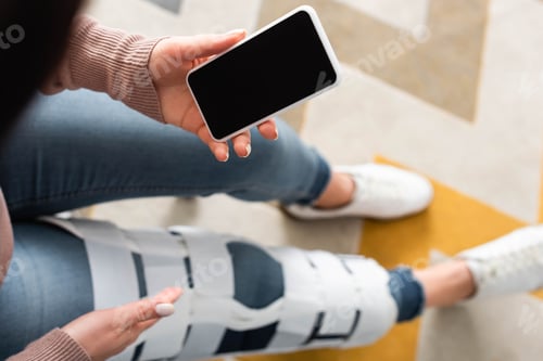 Preview: cropped view of woman with leg brace having online consultation with doctor on smartphone with blank