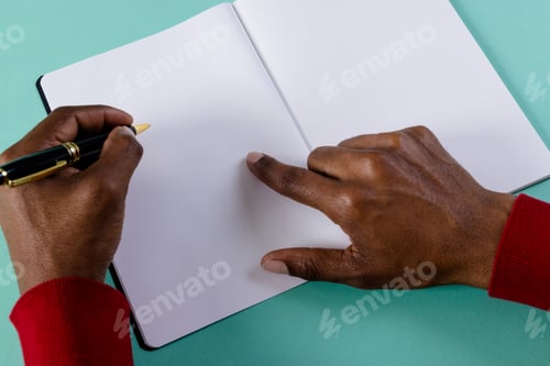 Preview: Hands of biracial man holding pen, writing in notebook with copy space on green background