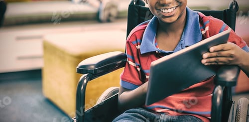 Preview: Disabled schoolboy on wheelchair using digital tablet in library