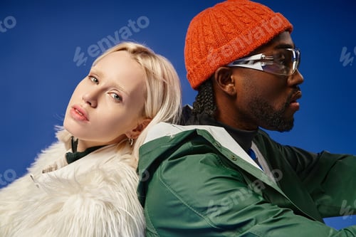Preview: multicultural models in trendy winter outfits posing together on blue backdrop, diversity and style