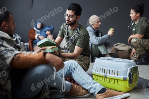 Preview: Volunteer Offering Food to Group Of Middle Eastern Refugees in Shelter