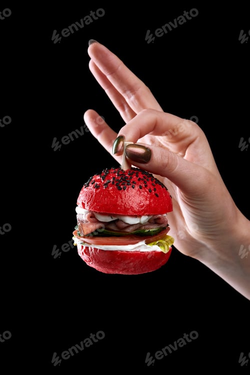 Preview: female hand holding mini burger as a Christmas tree toy on black background