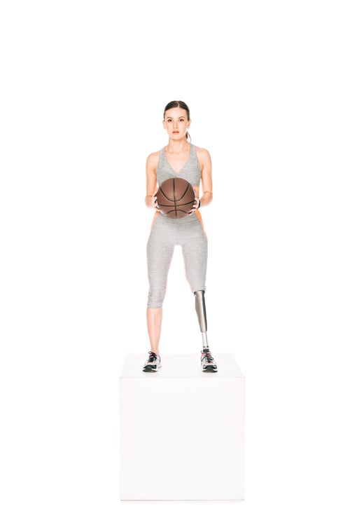 Preview: full length view of disabled sportswoman with prosthetic leg holding basketball ball isolated on